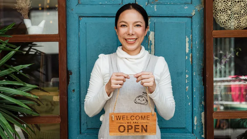 A café owner holding a 'We are open' sign at her shop door