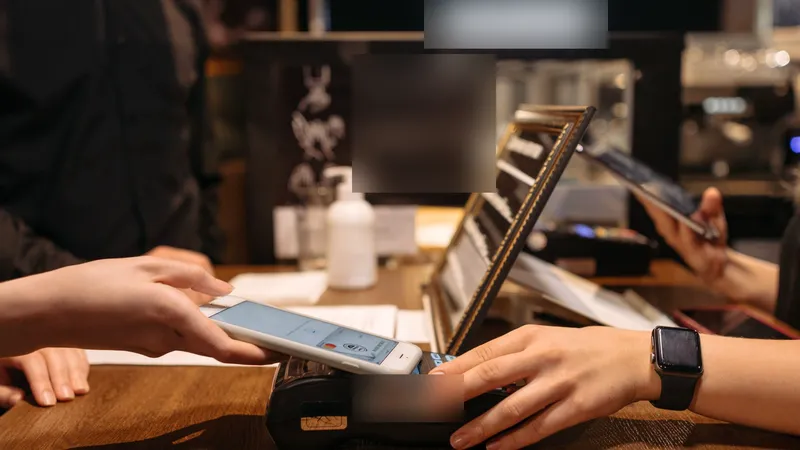 A customer tapping a phone on a card machine to pay at a café counter