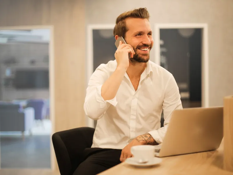 A broker smiling on a phone call at his laptop